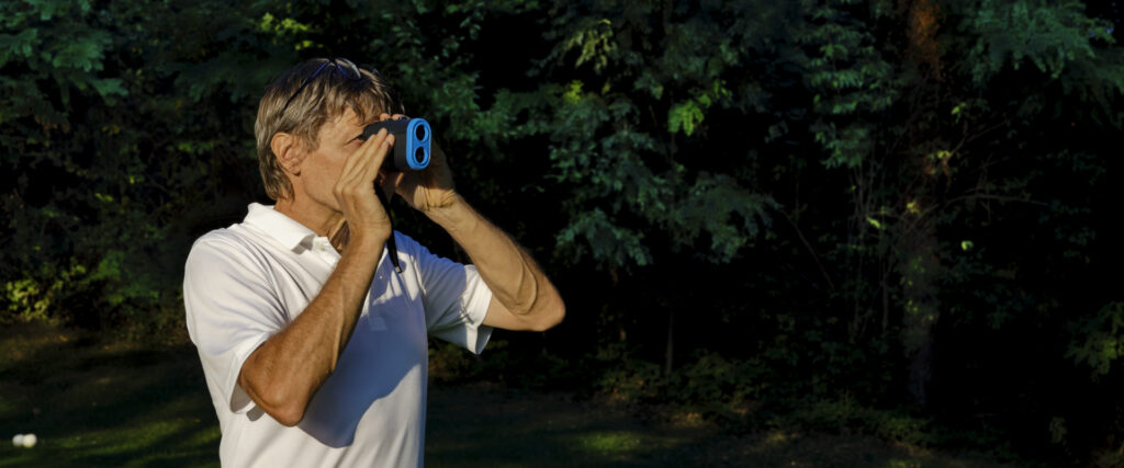 The golfer accurately measures the distance to the flag in a golf course with the laser rangefinder. 
