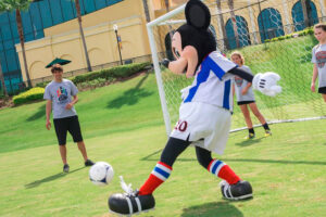 Mickey Mouse plays soccer with several youth players. 