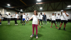 A group of youth soccer players standing hold soccer balls out in front of them. 