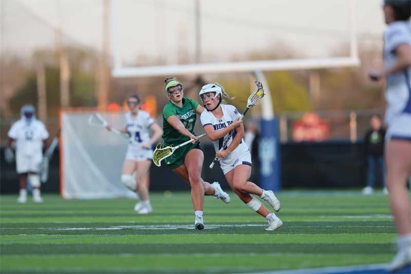 Courtesy National Association of Intercollegiate Athletics Two female lacrosse players fight for position on the field.
