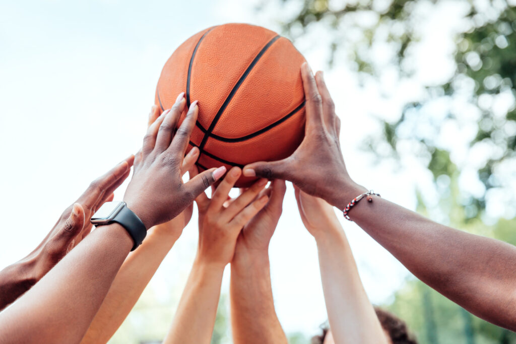 Several hands hold up a basketball in unison.
