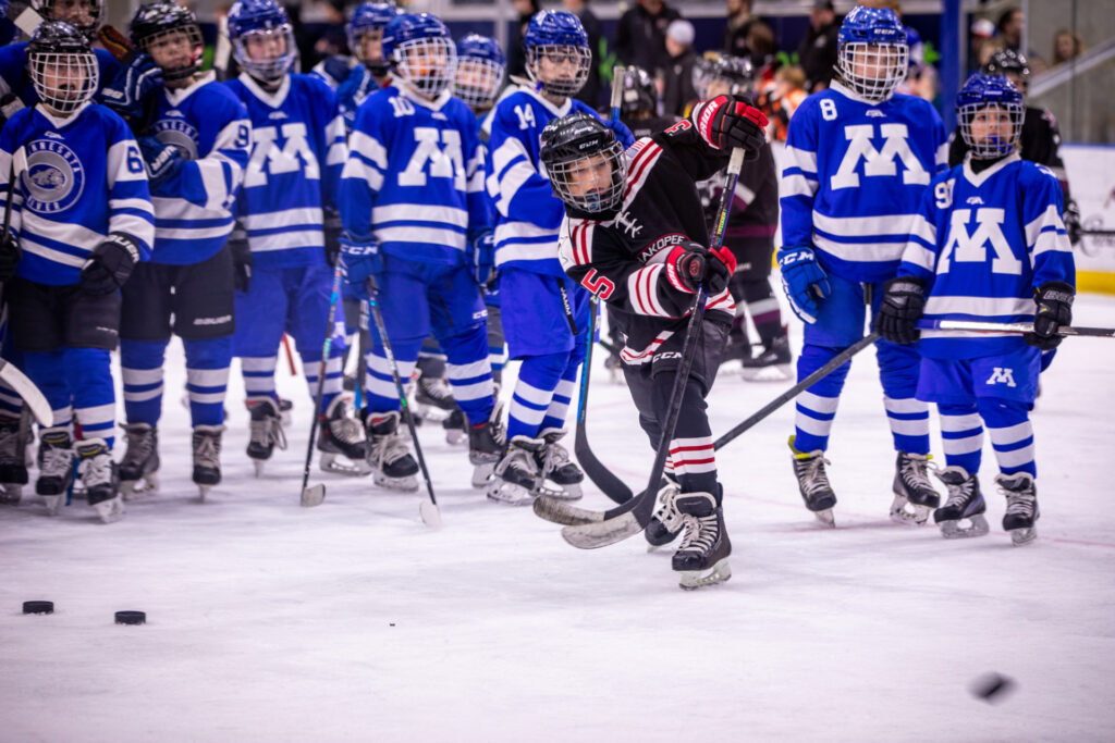 A young hockey player makes a penalty shot while the other team looks on.