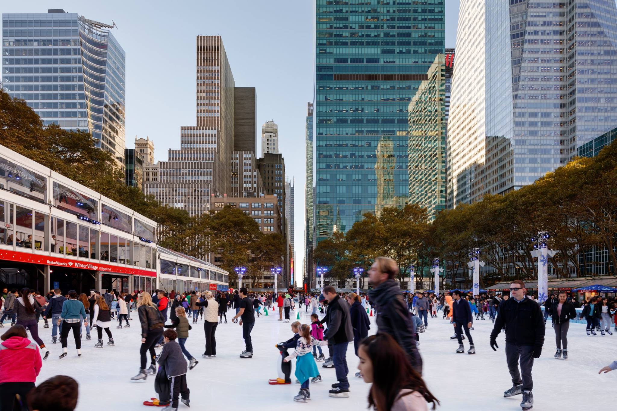 People skating on an outdoor ice rink surrounded by buildings.