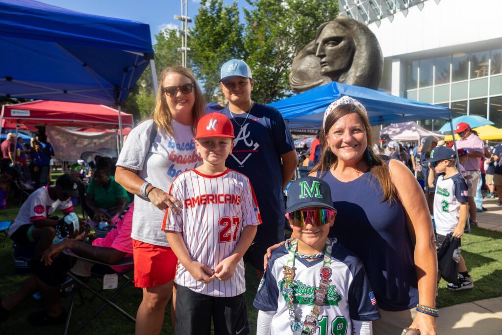 Two adult women and three boys in baseball uniforms stand in front of a statue at a baseball event in Baton Rouge.