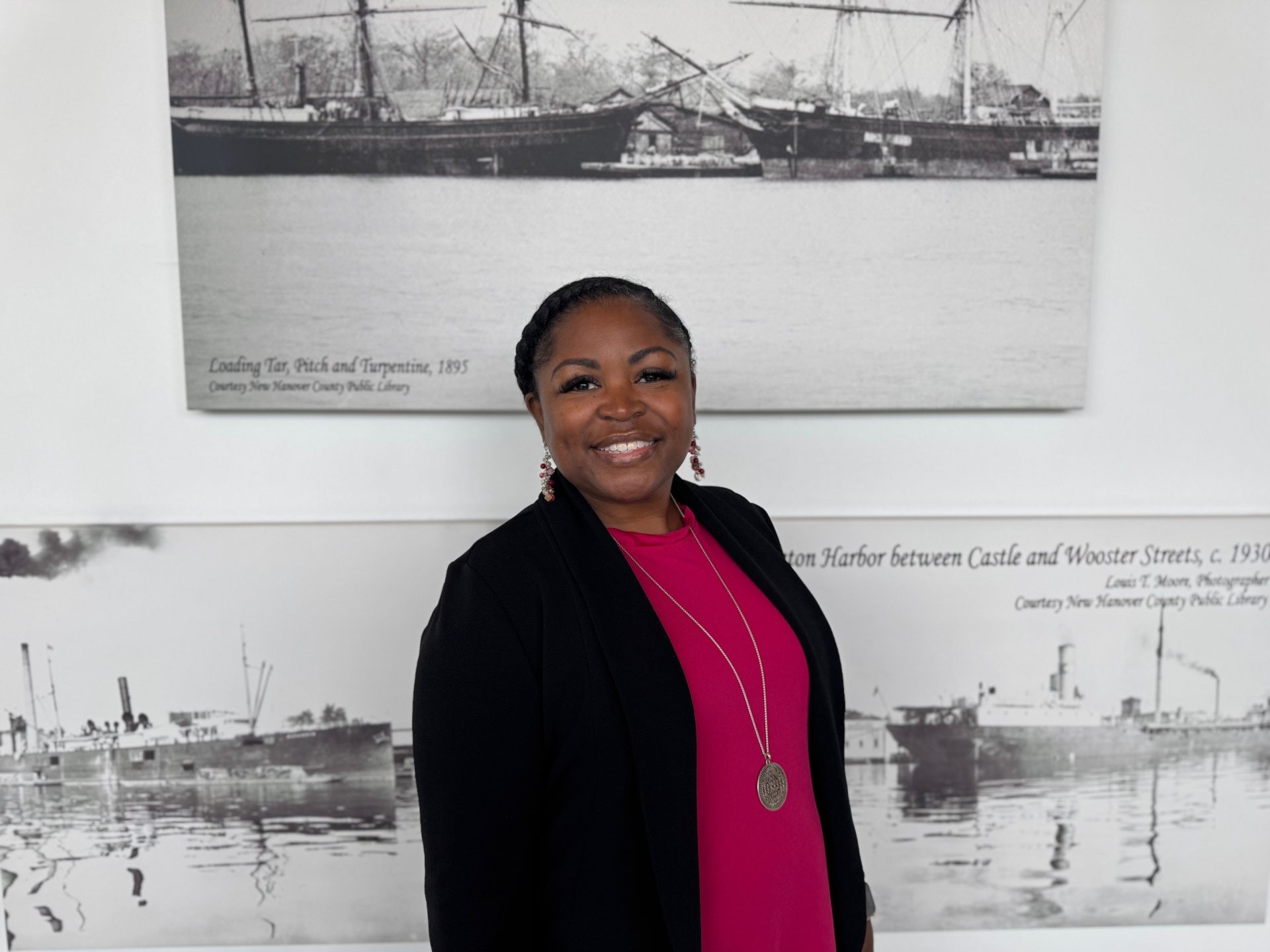 A headshot of Genia Artis wearing a black blazer and bright pink shirt.