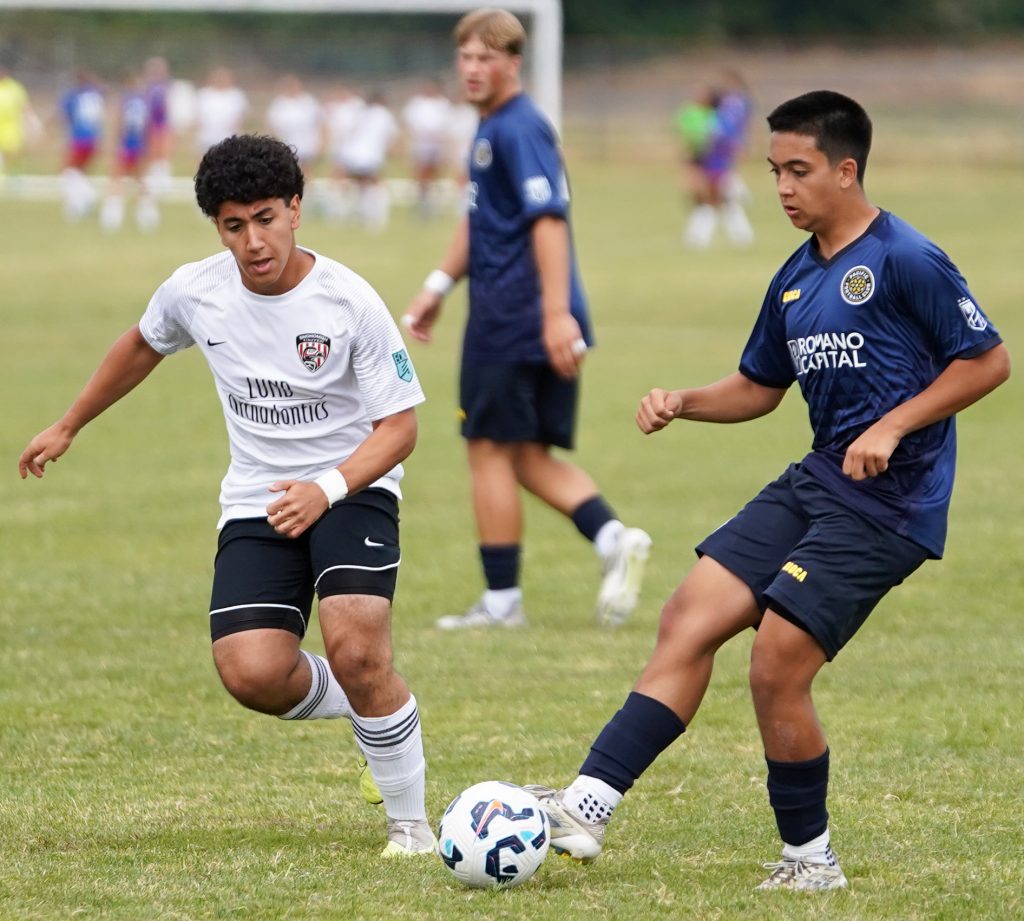 Two soccer players running for a ball on a field.