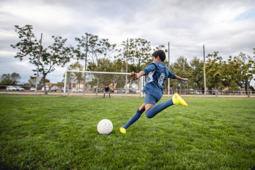 Rear view of a teenage boy kicking a soccer ball