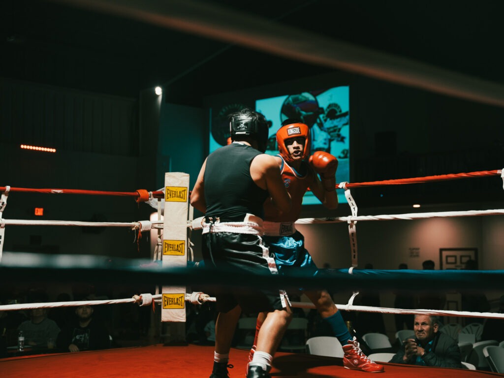 Two boxers, wearing head gear, square off against each other in the ring.