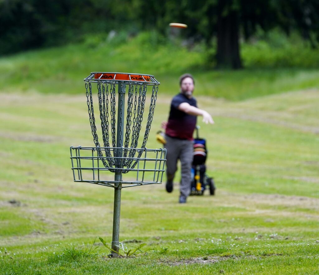 Disc golfer throwing a disc toward a chain link basket.
