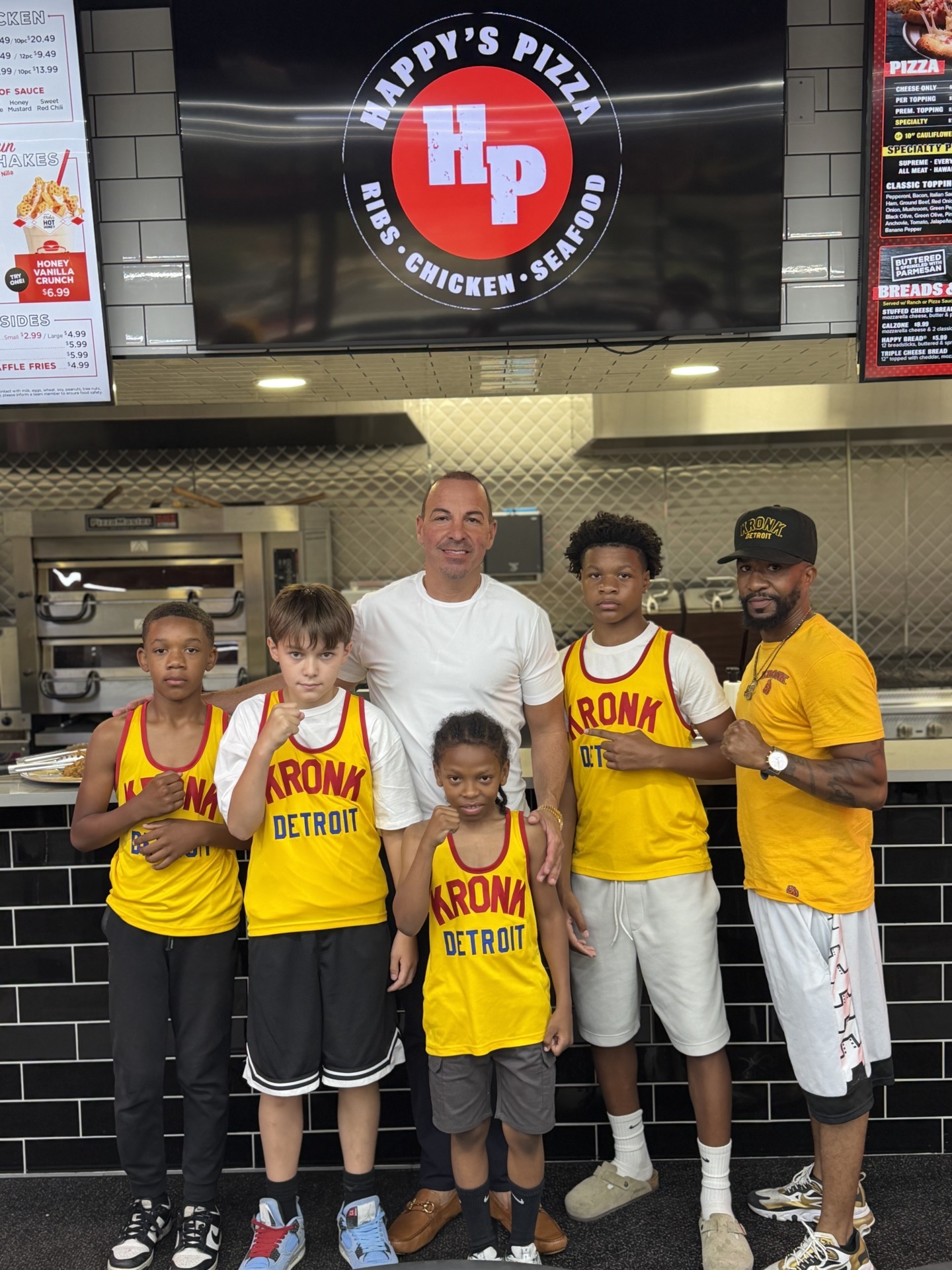 Happy Asker, Founder and CEO of Happy Group and Happy’s Pizza, with some of the boxers from the KRONK Amateur Boxing Team in their yellow jerseys. They’re standing in Happy’s Pizza store.