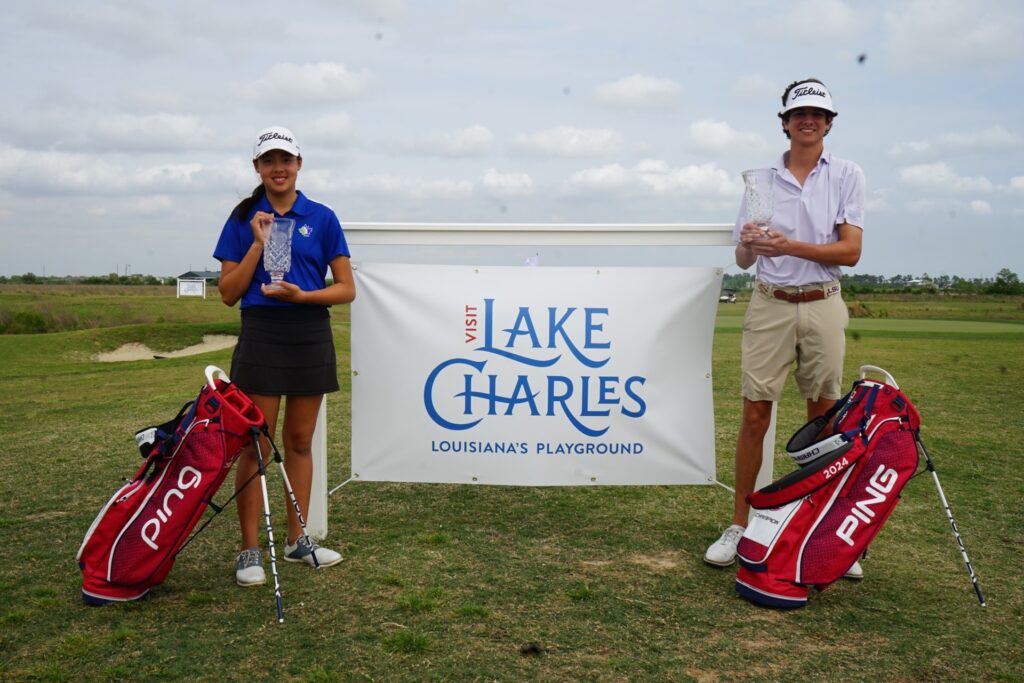 A pair of golfers stand in front of a Lake Charles Junior Championship sign