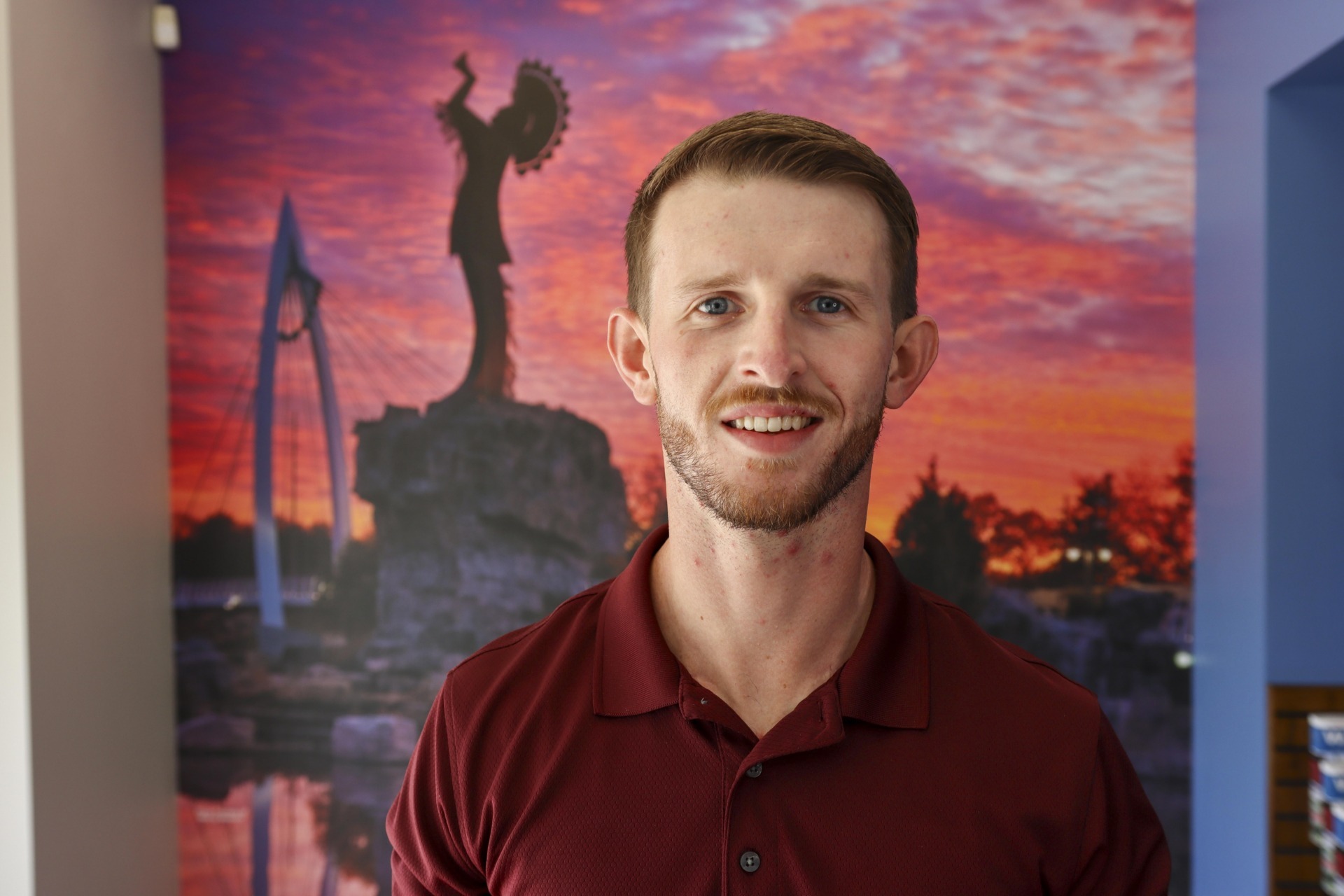 Spencer Olmstead smiles in a head-and-shoulders portrait, wearing a red polo shirt against a blurred, colorful background.